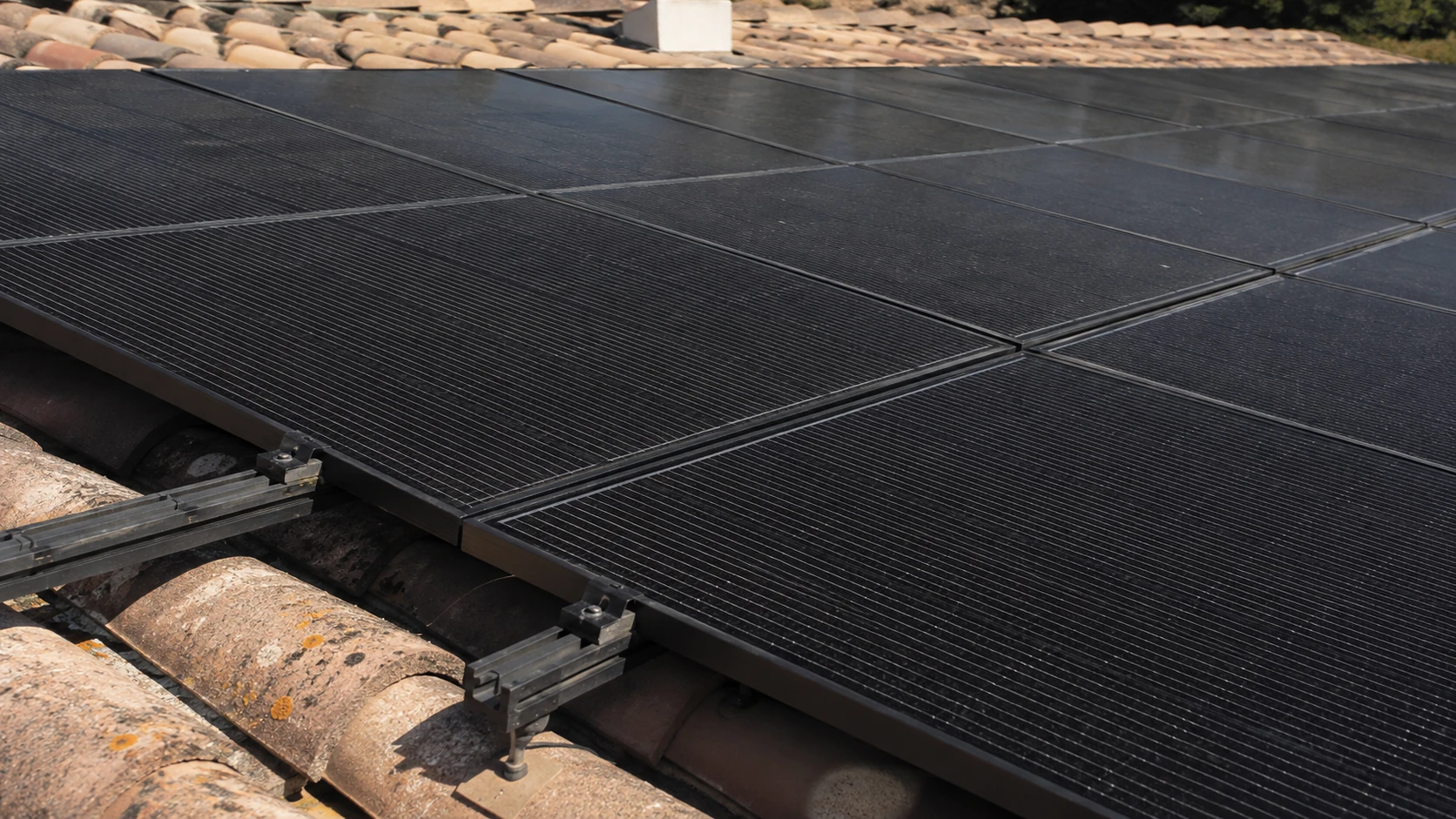Modules photovoltaïques noirs à cellules shingled posés sur rails aluminium au-dessus de tuiles canal, vus en lumière rasante.